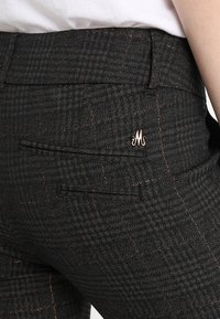 Svarta rutiga byxor med en texturerad tygkvalitet och subtila bronsefärgade detaljer. Inkluderar en bakficka och en liten metallisk logotyp.