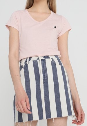 Femme portant un haut rose pâle à manches courtes et col en V, et une jupe en denim taille haute à rayures verticales bleues et blanches.