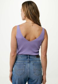 Fioletowy ribbed top na ramiączkach z szerokim dekoltem w kształcie litery V, zestawiony z wysokim stanem niebieskich dżinsów z dwiema tylnymi kieszeniami i detalami przeszyć.