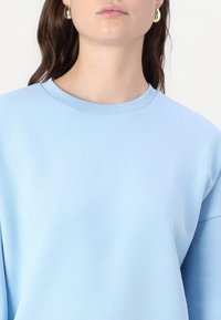 Sweatshirt bleu clair avec une texture douce, col rond et coutures d'épaules tombantes, présentant une coupe décontractée et un design simple.