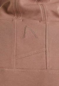 Gros plan sur un tissu marron avec des coutures cousues et une lettre stylisée subtilement brodée "A" sur le matériau.