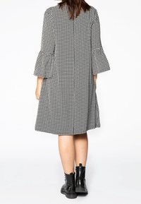 Černobílé šaty s vzorem houndstooth, s zvonovými rukávy, ke kolenům, vyrobené z jemné tkaniny. Nosit s černými šněrovacími kotníkovými botami.