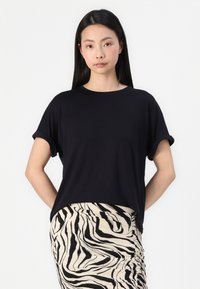 Zwarte T-shirt met korte mouwen en een relaxte pasvorm, met een ronde halslijn en opgerolde manchetten, gecombineerd met een beige en zwart gestreepte rok.