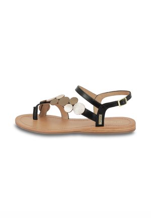 Sandali piatti neri con un design a ritaglio e accentuazioni in metallo circolare. La suola è color beige con una texture liscia e una cintura con fibbia.