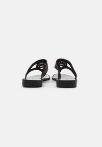 Svarta sandaler med en slät sula, som har en strukturerad remdesign och öppen baksida. Varumärket är präglat på sulan.