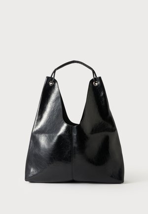 Sac à main en cuir noir brillant avec une seule poignée, corps structuré souple, et œillets métalliques fixant la poignée au sac.