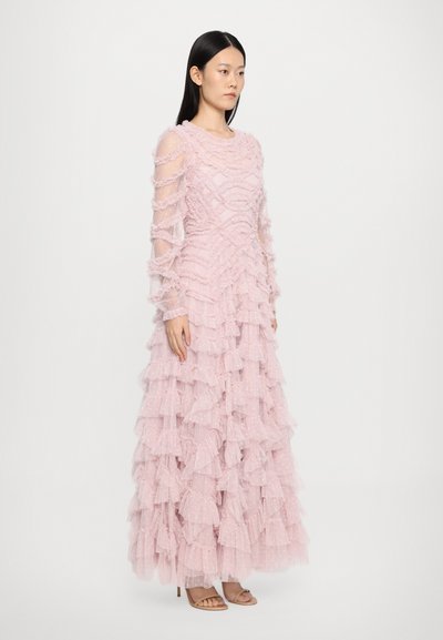 Lichtroze jurk met gelaagde ruches, gestructureerde stof, lange doorzichtige mouwen en een getailleerde bodice, gecombineerd met lichtgekleurde sandaaltjes met een hak.