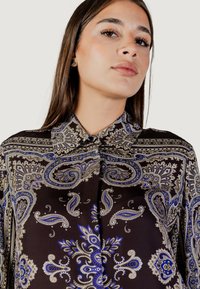 Blusa marrone a fantasia con motivi paisley blu, oro e bianco. Presenta un colletto e chiusura con bottoni, realizzata in un tessuto morbido.