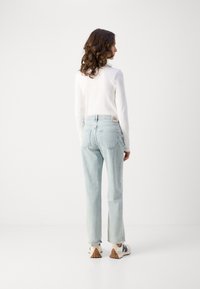 Lys blå høytlivsjeans med løs passform, med front- og baklommer. Brukt med en hvit langermet topp og sneakers.