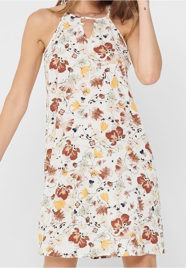 Femme portant une robe blanche sans manches avec un col halter et un imprimé floral multicolore dans des tons de brun, jaune et vert.