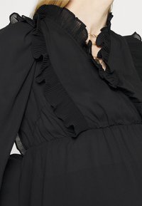 Vestido preto com decote e mangas em babados, feito de um tecido leve com textura plissada e cintura ajustada.