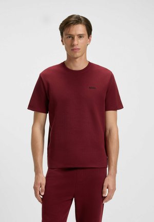 Burgunderfarbendes T-Shirt mit Rundhalsausschnitt aus strukturiertem Stoff, mit kurzen Ärmeln und einem kleinen schwarzen Logo auf der Brust.