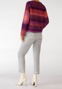 Stickad tröja i gradientnyanser av lila, rosa och röd, med en ribbad textur. Matchas med ljusgrå jeans och vita spetsiga klackar.