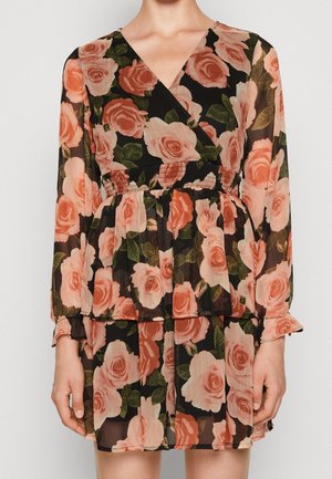 Robe longue à manches longues noire à fleurs avec des roses pêche et roses, des feuilles vertes, un col en V croisé et un détail de taille froncée portée par une personne debout.