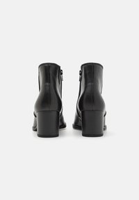 Bottines en cuir noir avec un bout arrondi, un talon rectangulaire et des zips latéraux. Texture lisse avec des détails de couture minimalistes.