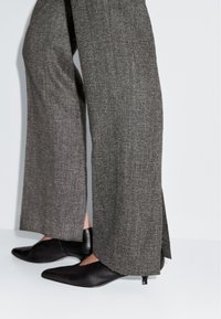 Szare, taliowane spodnie o wysokim stanie z teksturowanej tkaniny, z bocznym rozcięciem i w połączeniu z czarnymi, szpiczastymi szpilkami.