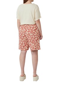 Top corto a maniche corte di colore avorio abbinato a pantaloni corti color mattone con un motivo bianco irregolare. La modella indossa sandali con zeppa beige.
