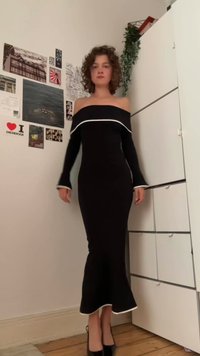 Svart off-shoulder klänning med vit kantning, långa ärmar och en figurnära silhuett. Utsågad nederkant ger struktur. Bärs med svarta högklackade skor.
