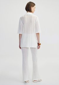 Witte gebreide twee-delige outfit met een losse top met korte mouwen en flared broek, voorzien van een ribbelstructuur en zijsplitten.