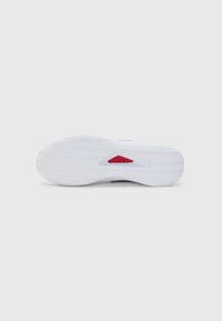Suela de zapatilla blanca con un patrón de relieve en espiga, con un acento rojo cerca del arco y una forma redondeada para mejorar la tracción.