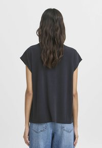 Schwarzes T-Shirt mit kurzen Ärmeln aus weichem Stoff, mit lässigem Schnitt und geradem Saum, kombiniert mit hellblauen Denim-Jeans.