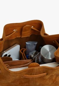 Brown suede handbag with a soft texture, open top, and inner compartments containing a phone, tubes, keys, and a dark bottle.
