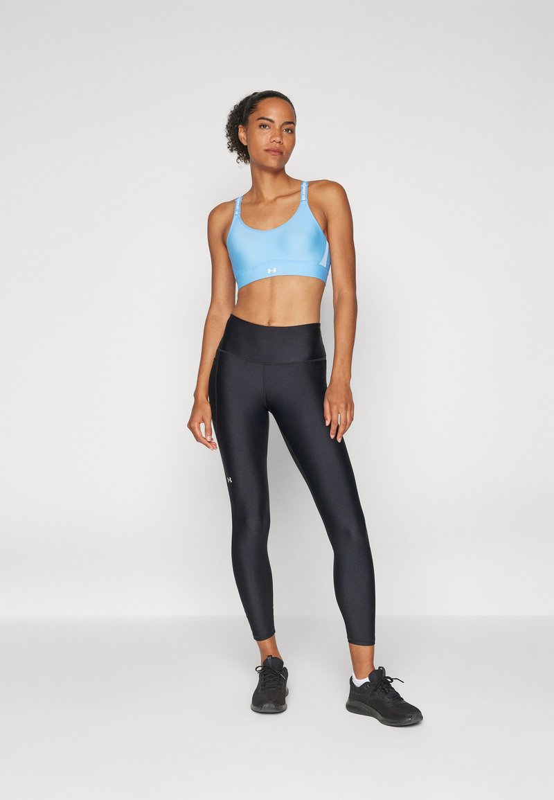 Reggiseno sportivo azzurro chiaro con spalline a contrasto, abbinato a leggings neri a vita alta. Entrambi sono realizzati in materiale elastico. Sneakers nere.