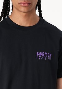 Zwart t-shirt van katoen, voorzien van een klein paars grafisch logo op de linkerkant van de borst. Ronde hals en korte mouwen.