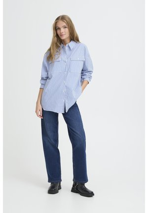 Gestreiftes blaues und weißes Hemd mit Knopfverschluss und zwei Brusttaschen; kombiniert mit dunkelblauen weiten Jeans und schwarzen Stiefeletten.
