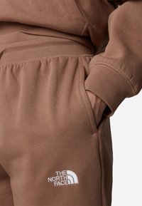 Bruna sweatpants gjorda av mjukt tyg med en avslappnad passform, med elastisk midja, sidofickor och en vit logotyp på benet.