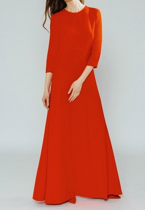 Femme portant une longue robe orange vif à manches trois-quarts, debout devant un fond clair et uni.