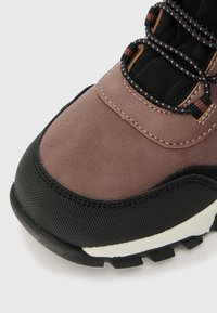 Brūni pārgājienu apavi ar strukturētu melnu gumijas zoli, pastiprinātu purngali un kontrastējošu izšuvumu. Aprīkoti ar drošu auklu sistēmu.