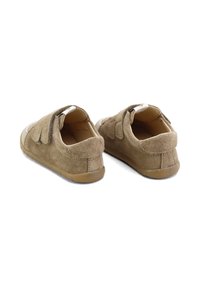 Zapatos de ante marrón con un diseño bajo, que incluyen correas de velcro, punta redondeada y suela de goma. La textura es suave y lisa.