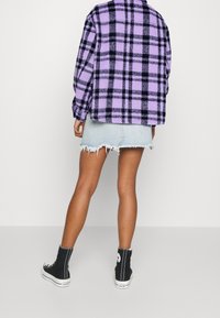 Fialová a černá kostkovaná flanelová bunda přes světle modrou mini sukni s třepeními, doplněná černými vysokými teniskami.