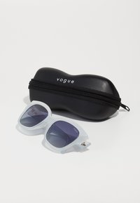 Ochelari de soare supradimensionați cu rame de culoare albastru deschis și lentile gri închise, alături de o husă neagră cu fermoar, pe care se află textul 'vogue'.