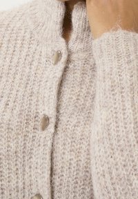 Cárdigan de punto beige con un cuello alto, tejido texturizado y botones redondos de color claro a lo largo del frente.