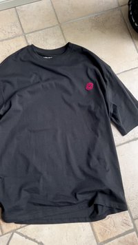 Camiseta de algodón negra de manga corta, con un detalle bordado de labios rosas en el lado izquierdo del pecho, textura suave y corte relajado.