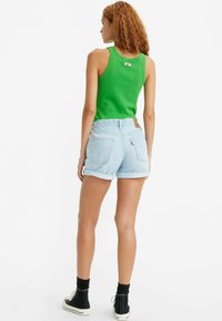 Top sin mangas verde combinado con pantalones cortos de mezclilla azul claro, con dobladillos enrollados, una etiqueta en la parte posterior y zapatillas negras de caña alta.