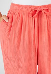 Pantalons en corail, souples et ondulés, avec une taille élastique et un cordon de serrage. Leur texture comporte des poches latérales et un tissu texturé pour un maximum de confort.