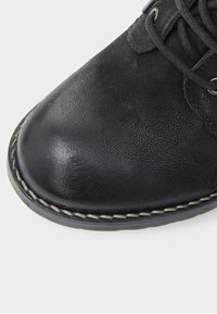 Zapato de cuero negro con punta redondeada, que presenta una parte superior texturizada, costuras en contraste a lo largo de la suela y cordones para un ajuste seguro.