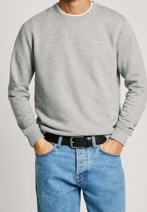 Grijze sweatshirt met geribbelde manchetten en halslijn, voorzien van een klein wit logo op de borst, gecombineerd met lichtblauwe jeans en een zwarte riem.