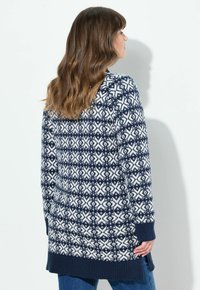Granatowy sweter z dzianiny z białymi geometrycznymi wzorami, długimi rękawami, ściągaczami na mankietach i u dołu, z nieco dłuższym tyłem.
