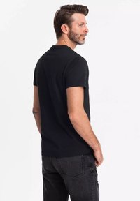 Sort kortærmet t-shirt med rund hals, lavet af blødt stof, parret med mørkegrå slidte jeans, der har baglommer.