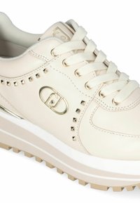 Beige leren sneaker met studaccenten, ronde neus en witte buitenzool. Heeft een gouden logo en platte veters voor een veilige pasvorm.