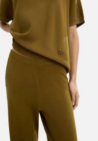Dopasowany dzianinowy zestaw składający się z oliwkowo-zielonej bluzki luźnego kroju z widocznym logo oraz spodni prostych o gładkiej fakturze.