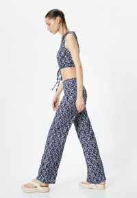 Blauw gemusterd crop top met knoop en bijpassende wijde broek. Lichtgewicht stof met een ruitpatroon. Casual sandalen maken de look compleet.