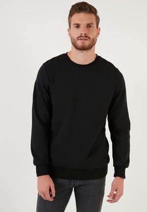 Zwarte crewneck sweatshirt met ribgebreide boorden en onderrand, gemaakt van textuurstof, gedragen over donkere jeans, met een relaxte pasvorm.