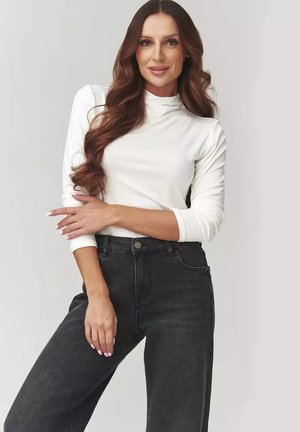 Biała bluzka z długim rękawem i wysokim kołnierzem, zestawiona z czarnymi jeansami o wysokim stanie. Gładka tekstura i dopasowany krój.