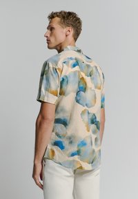 Kortebloezem shirt in lichtbeige stof, met een aquarelpatroon in blauw en groene tinten. Minimalistisch ontwerp met een klassieke kraag.