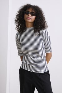 Zwart-wit gestreepte ribbeltop met korte mouwen en gegolfde randen, gecombineerd met zwarte broeken en rechthoekige zonnebril.